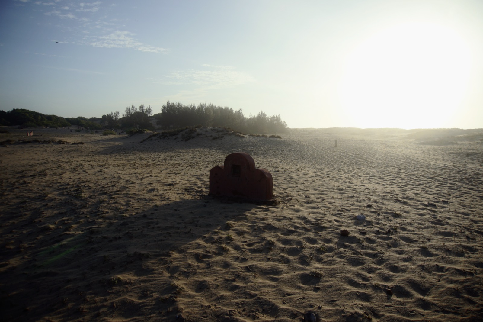 A weathered red shrine standing alone on a sunlit sand dune